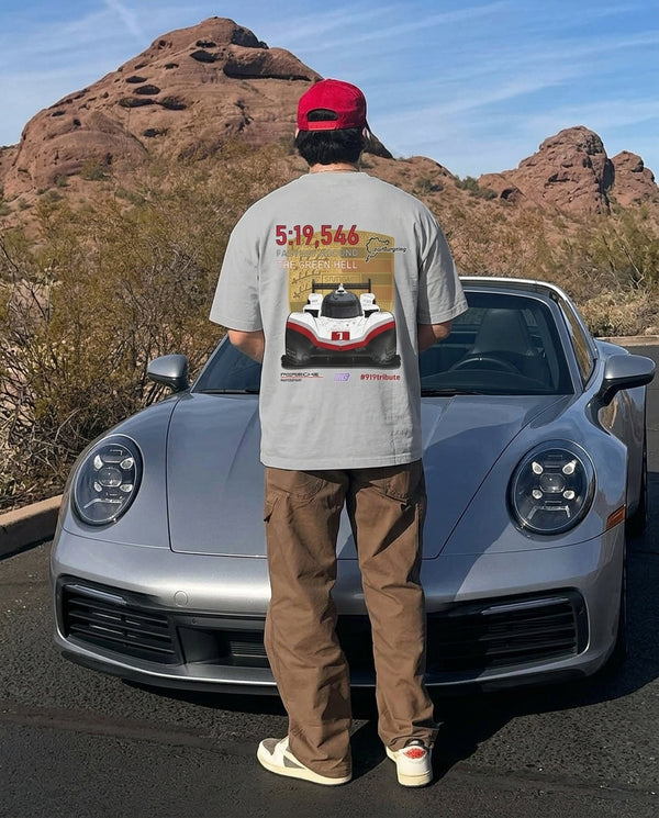 Man in a grey 919 Hybrid Evo oversized tee facing a silver Porsche 911 in the desert, back print visible