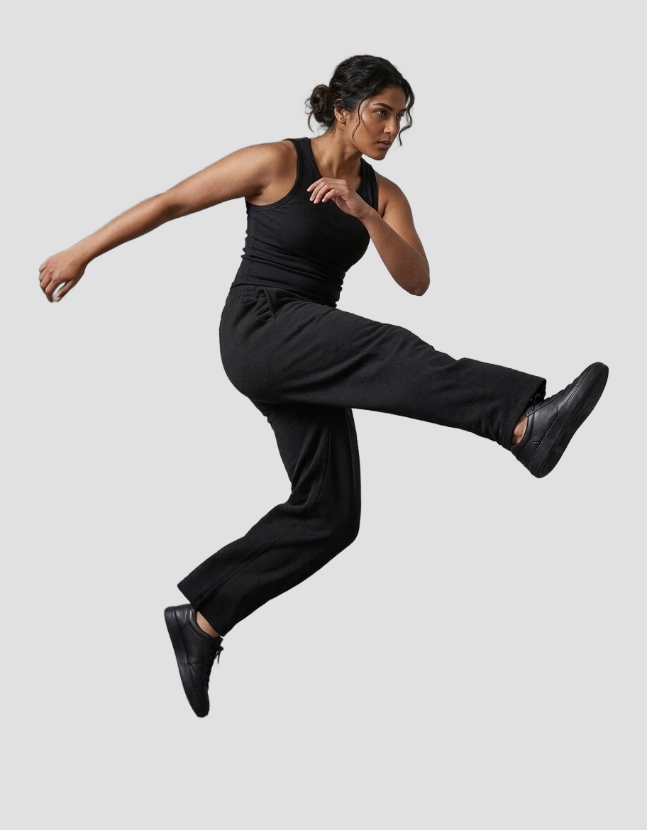 Woman mid-jump wearing black MotorBae MB Essentials sweatpants with a black tank top